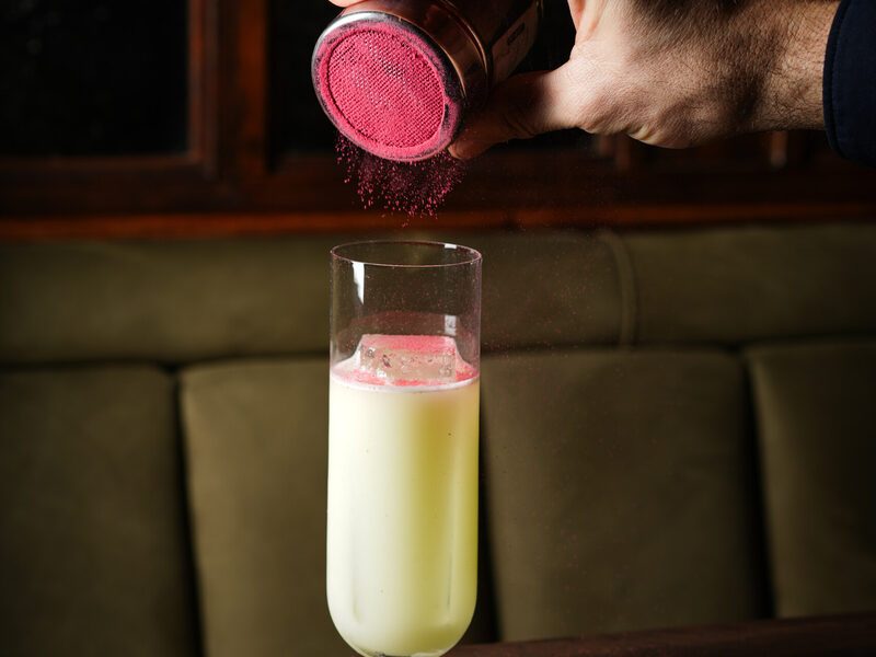 A cocktail being finished with raspberry powder