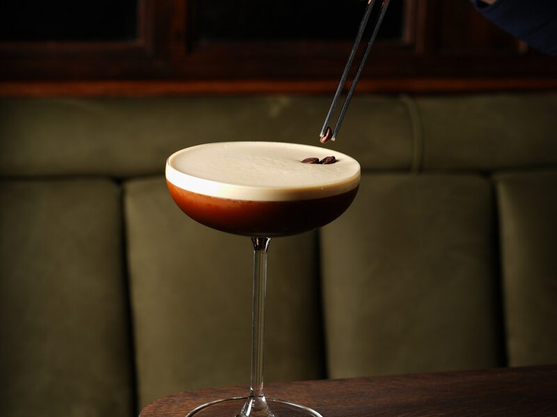 An espresso martini receiving its coffee bean garnish