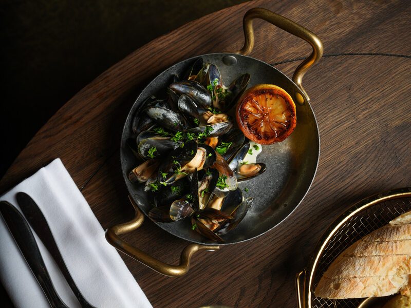 Mussels in a copper pan with grilled lemon and baguette