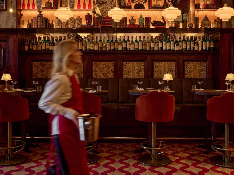 The Chez van Rijn dining room with its backlit curiosity wall and staff in bordeaux aprons
